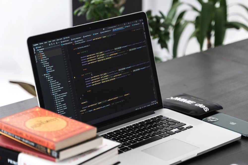 Laptop with programming code open on the screen, surrounded by books and a tidy desk