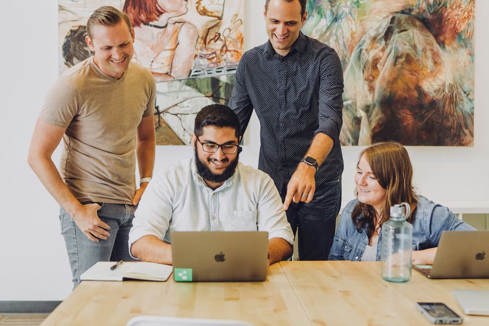 Group of professionals collaborating in a modern work environment, focused on a laptop screen