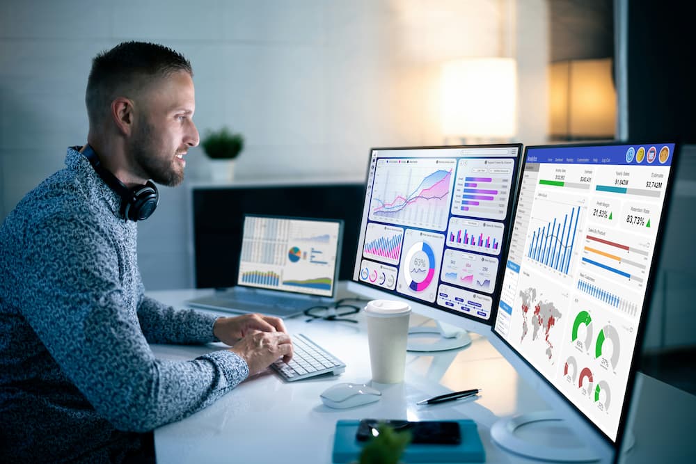 Man analyzing charts and data on multiple monitors, presenting business and performance information