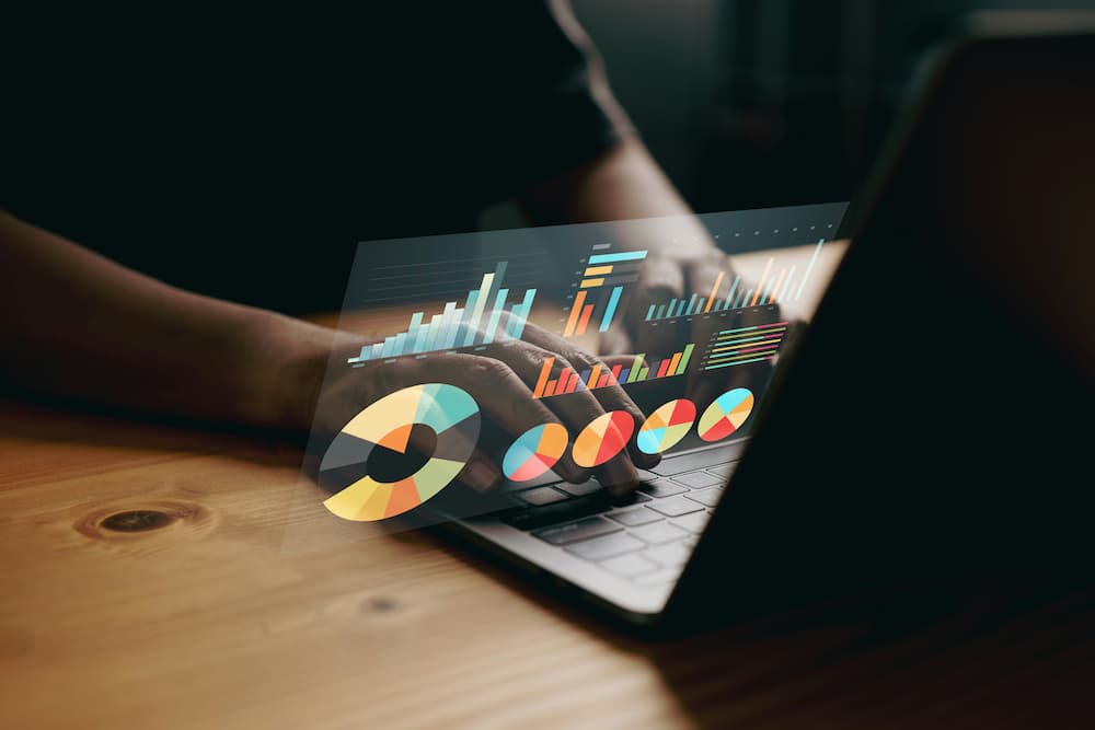 "A person is working on a laptop with various colorful data visualizations projected above the keyboard. The visualizations include bar charts, line graphs, and pie charts, which likely represent analytical data for a law firm.