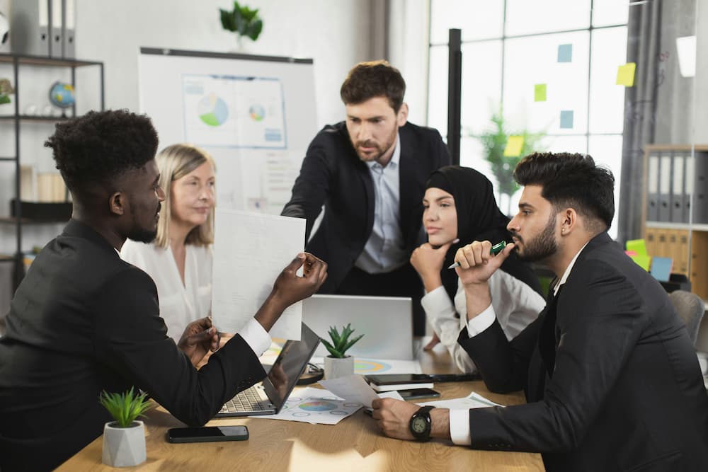 A group of lawyers in formal attire are engaged in a discussion around a conference table in a modern office setting.