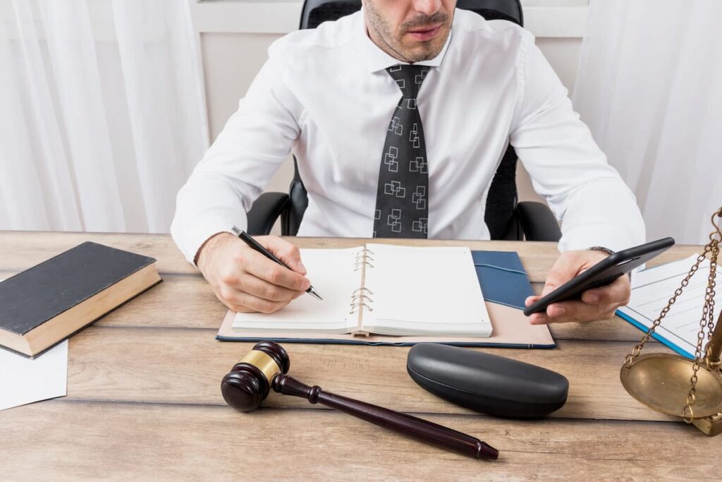 Lawyer using phone and taking notes at desk with legal items, focused on law firm accounting.